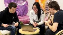 Three people sit around a laptop looking at the screen