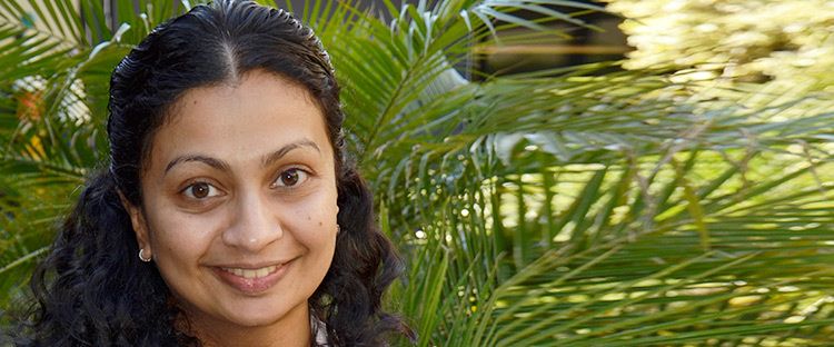 Female with light brown skin and dark brown hair smiling at the camera
