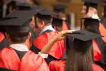 A group of students dressed in regalia await their graduation ceremony