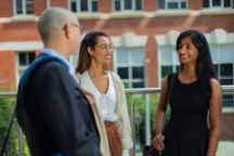 Three professional dressed people, two female and one male, smiling and chatting.
