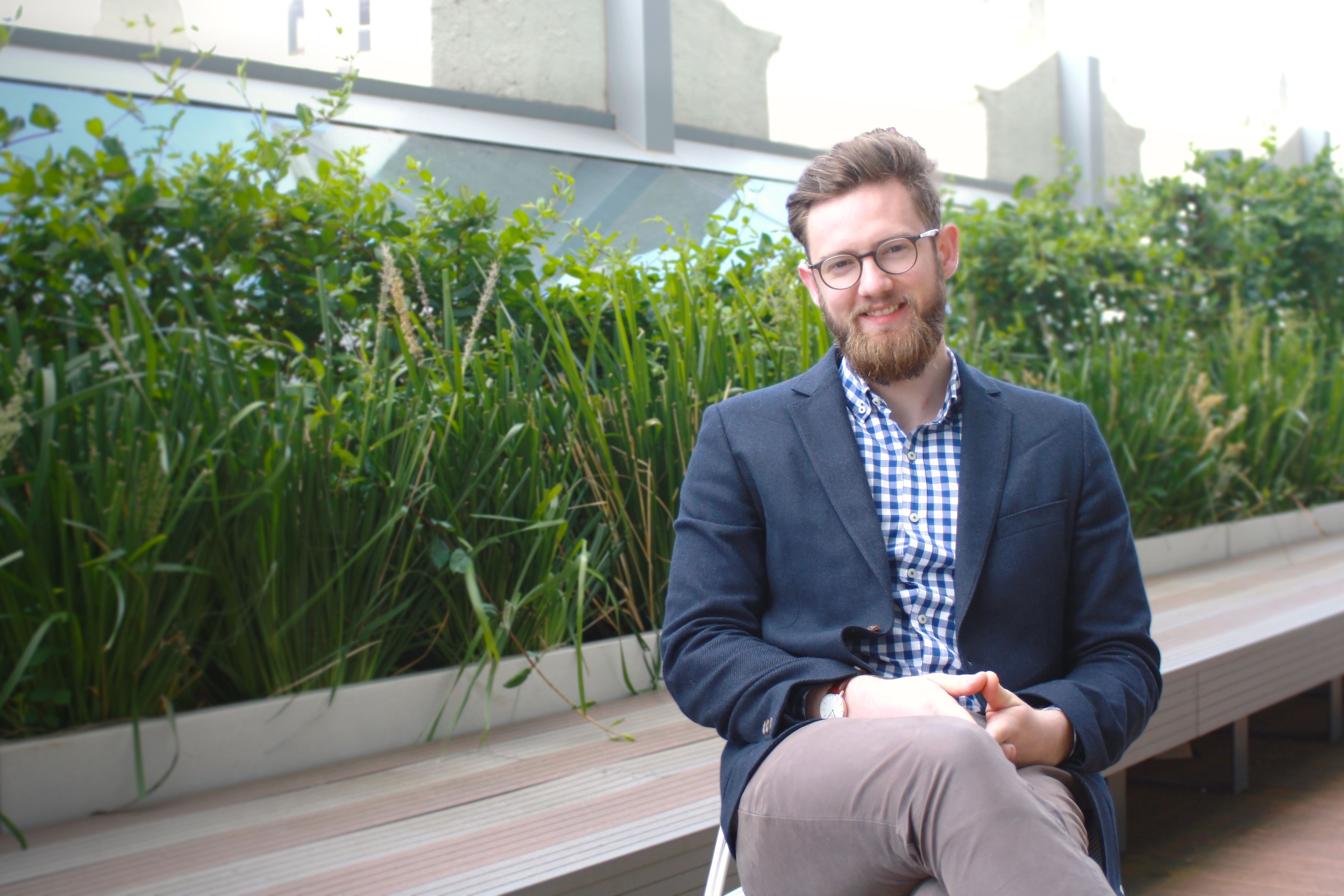 James Hanely sits relaxed with legs crossed in front of a green garden bed