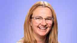 Jen Sharpe is smiling at camera and wears reading glasses.