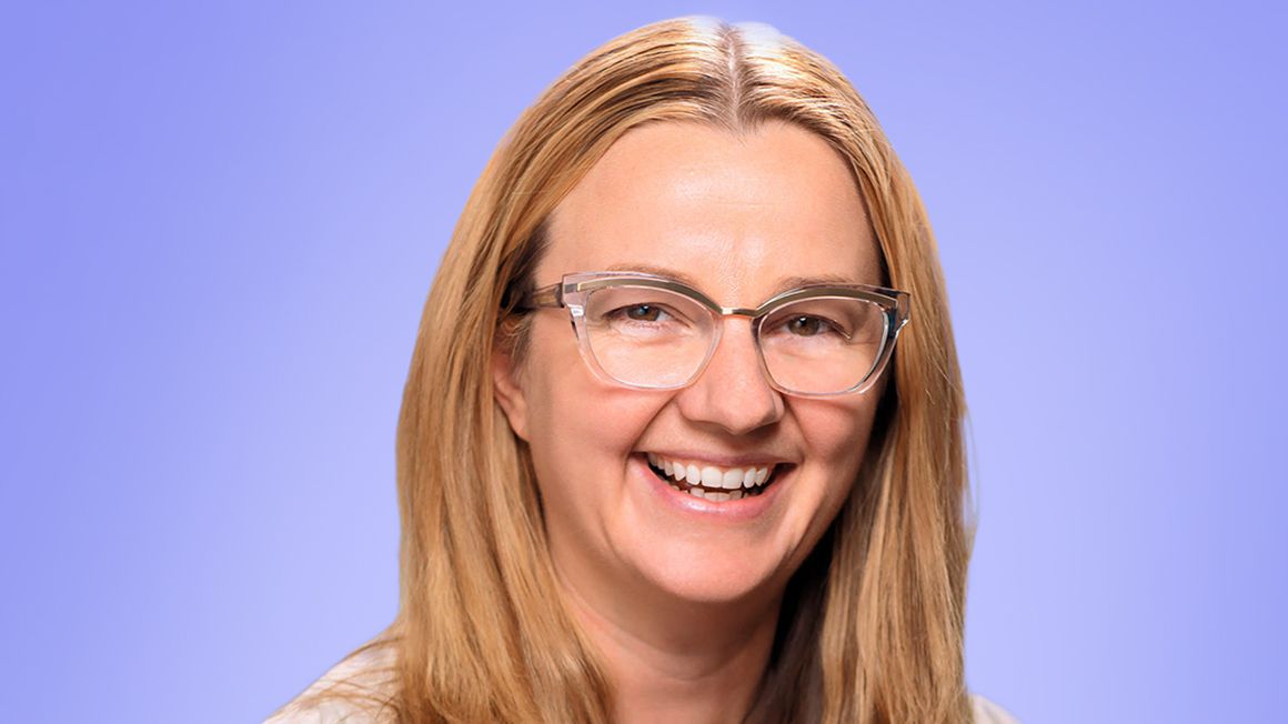 Jen Sharpe is smiling at camera and wears reading glasses.