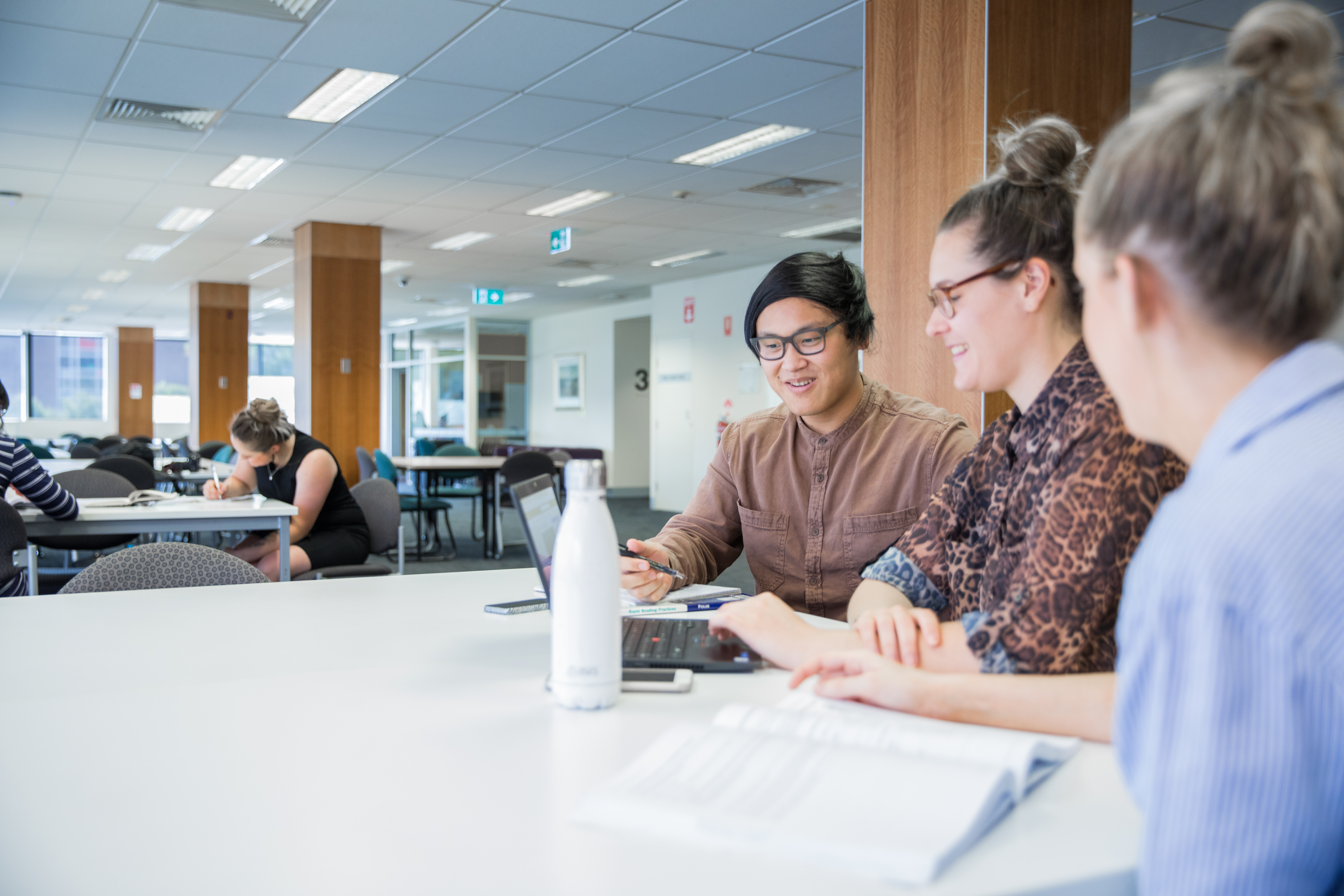 Three people sitting at a table looking at a laptop