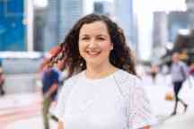 Young female student wearing a white top smiles to camera outside on a sunny day