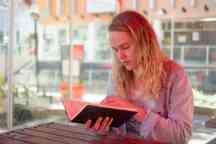 Female student sits outside reading a book at table