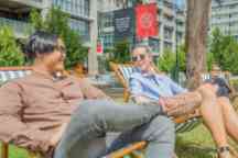 Students sit on deck chairs in the sun in Wakefield Gardens as they chat and smile