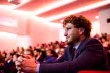 Student leans forward in an amphitheatre, hands clasped