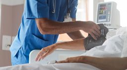 A healthcare worker checking a patient's blood pressure on a hospital bed.
