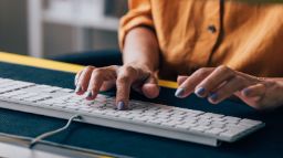 Close-up shot of a woman's hands typing using a computer keyboard on a desk