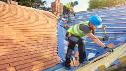 Construction workers on roof fitting new roof tiles.