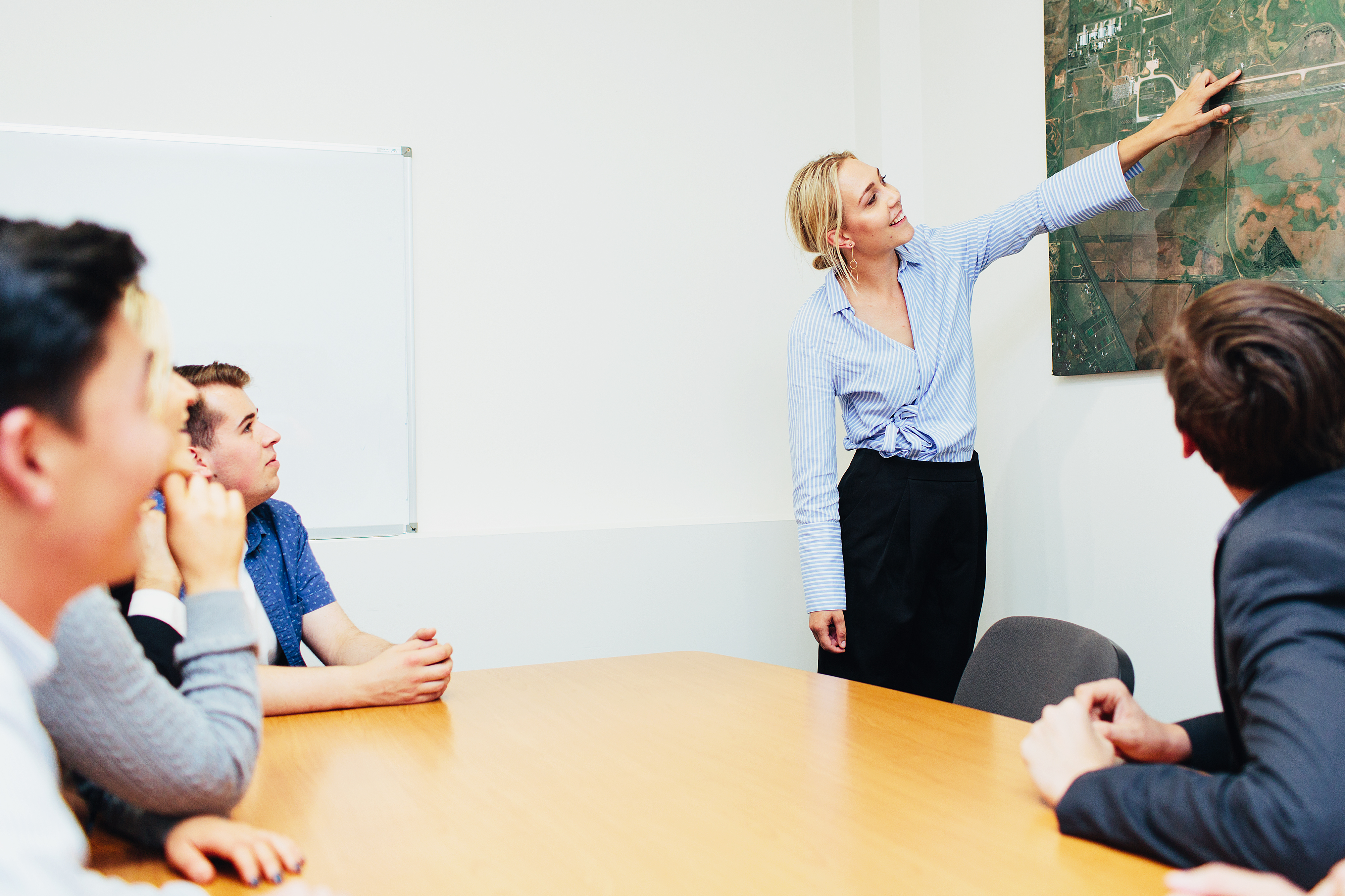 Aviation students sitting around a table watching another student points out something on a map on the wall