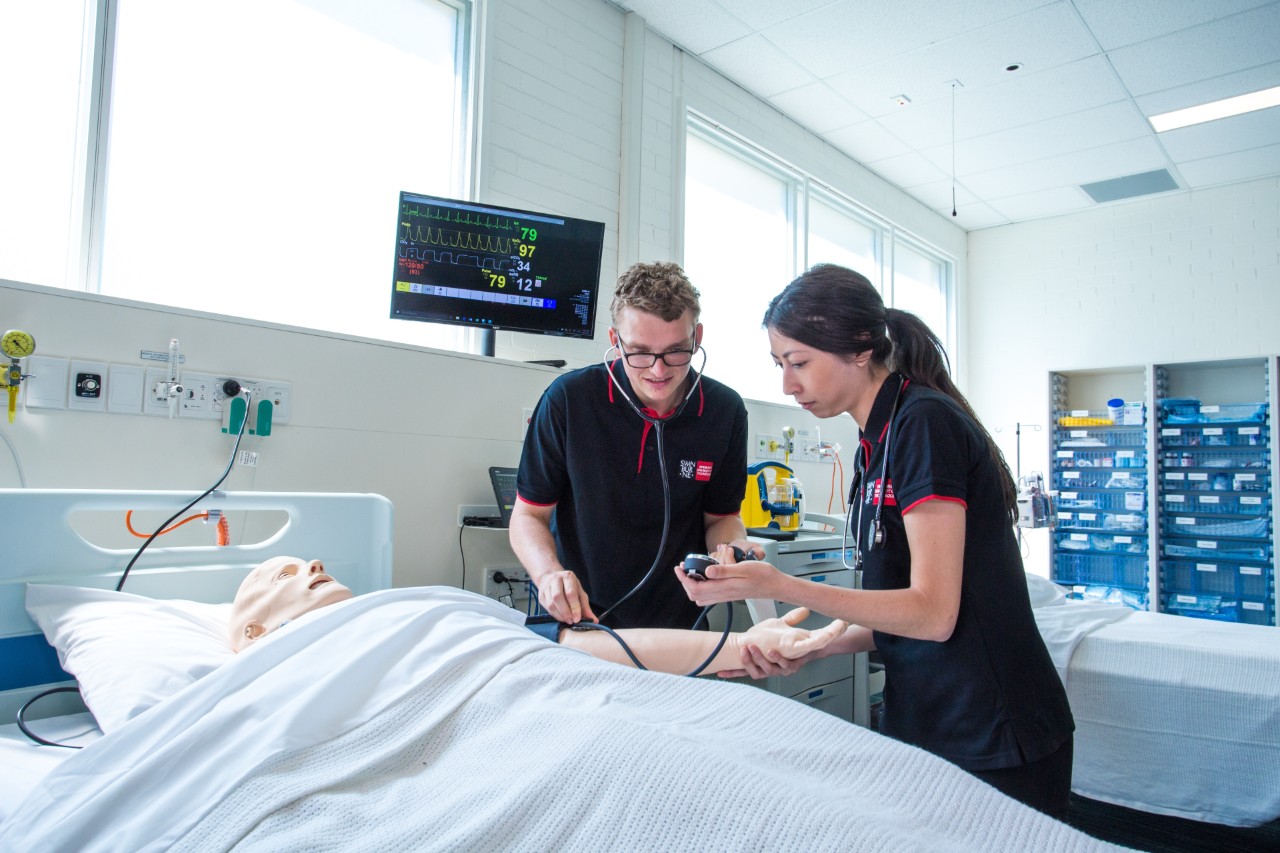 Two nursing students practice using hospital equipment in the Hawthorn nursing labs