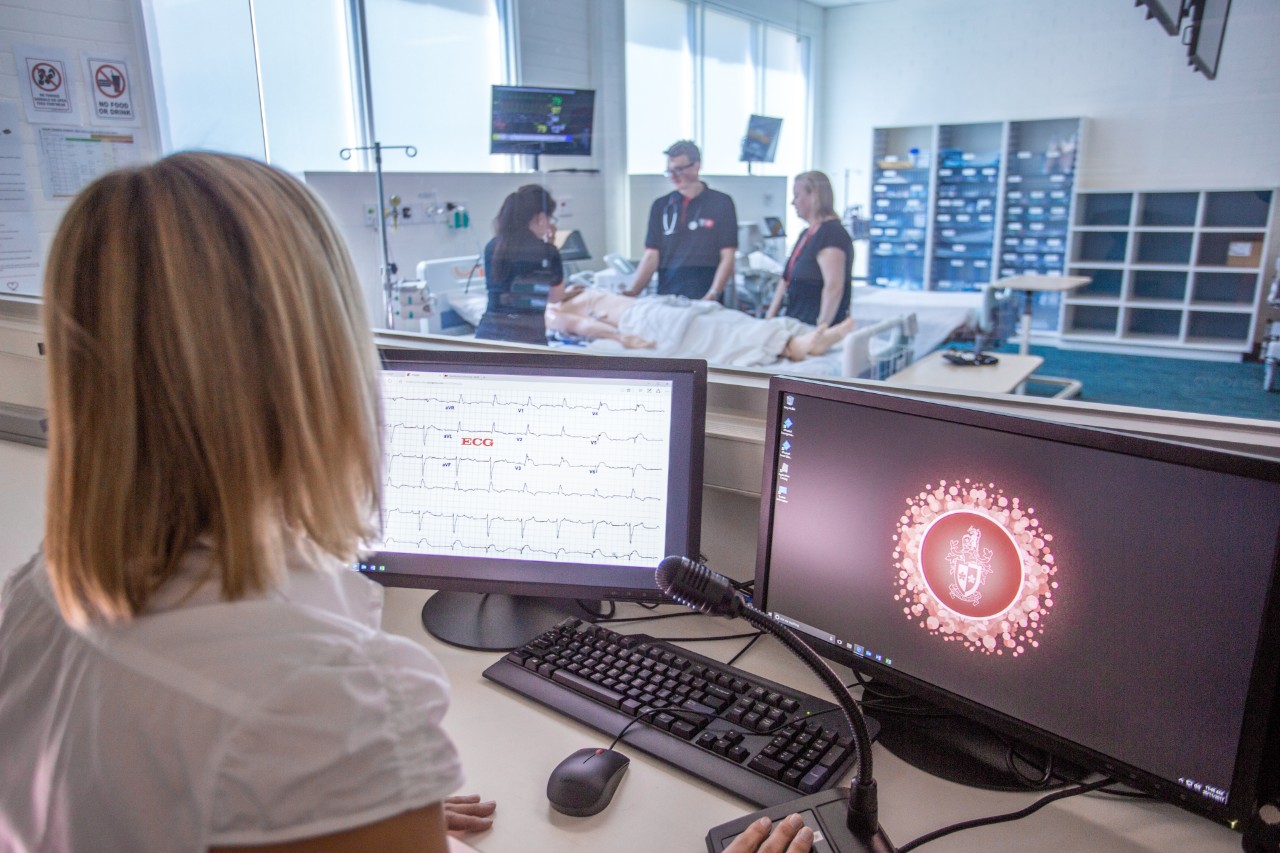 Woman overseas three nursing students tending to dummy patient at Swinburne's nursing lab
