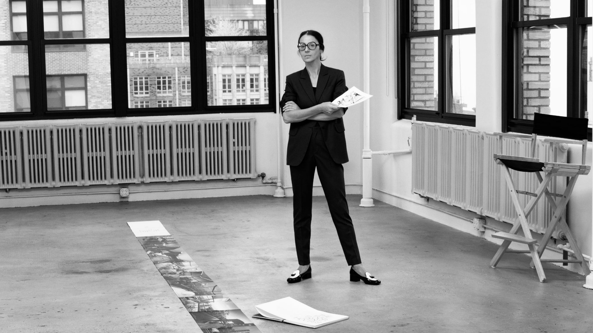 A black and white shot of Visnja standing, arms crossed in a cavernous NYC warehouse. She is laying out designs for the Penthouse Book Construction